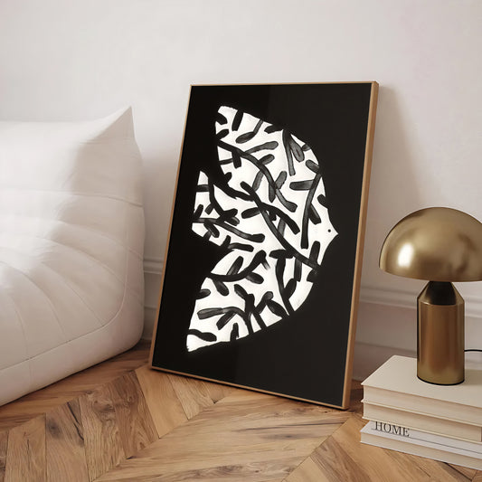 Framed abstract art piece on a wooden floor with a lamp and books in the background.