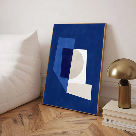 Abstract art print on a wooden floor with a lamp and books in the background