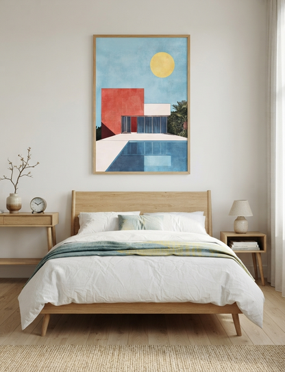 A framed Bauhaus style swimming pool architectural print with Palm Springs house hangs above a light wood bed in a bright, modern bedroom. The artwork features a blue sky, a yellow sun, a red geometric building, and a blue pool, all enclosed in a thin natural wood frame.