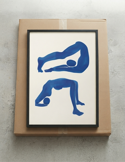 Framed Modern Abstract Art for Bedroom Sanctuary by PrintHaus featuring two blue silhouetted human figures in yoga or stretching poses on an off-white background, displayed on a brown cardboard box against a light gray textured wall.