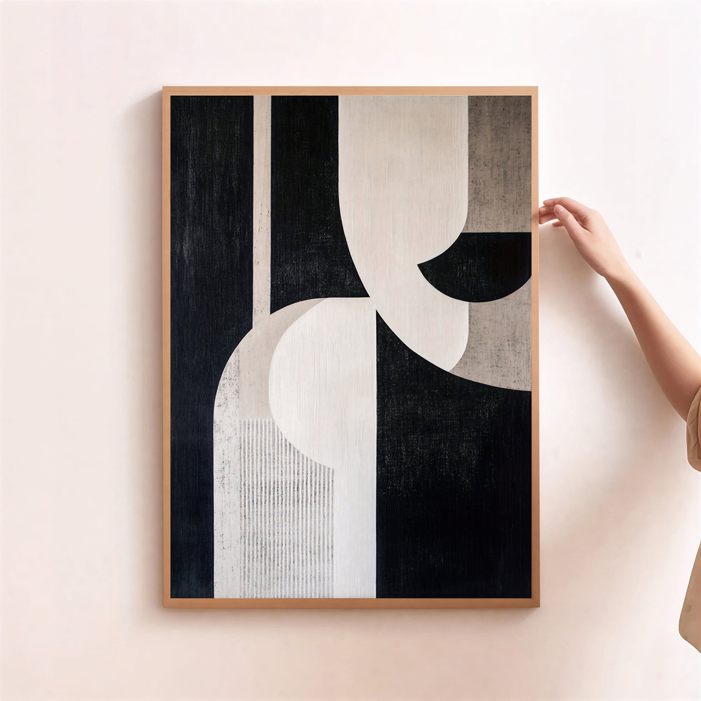 Abstract art print with black, white, and beige shapes in a wooden frame on a light pink wall.