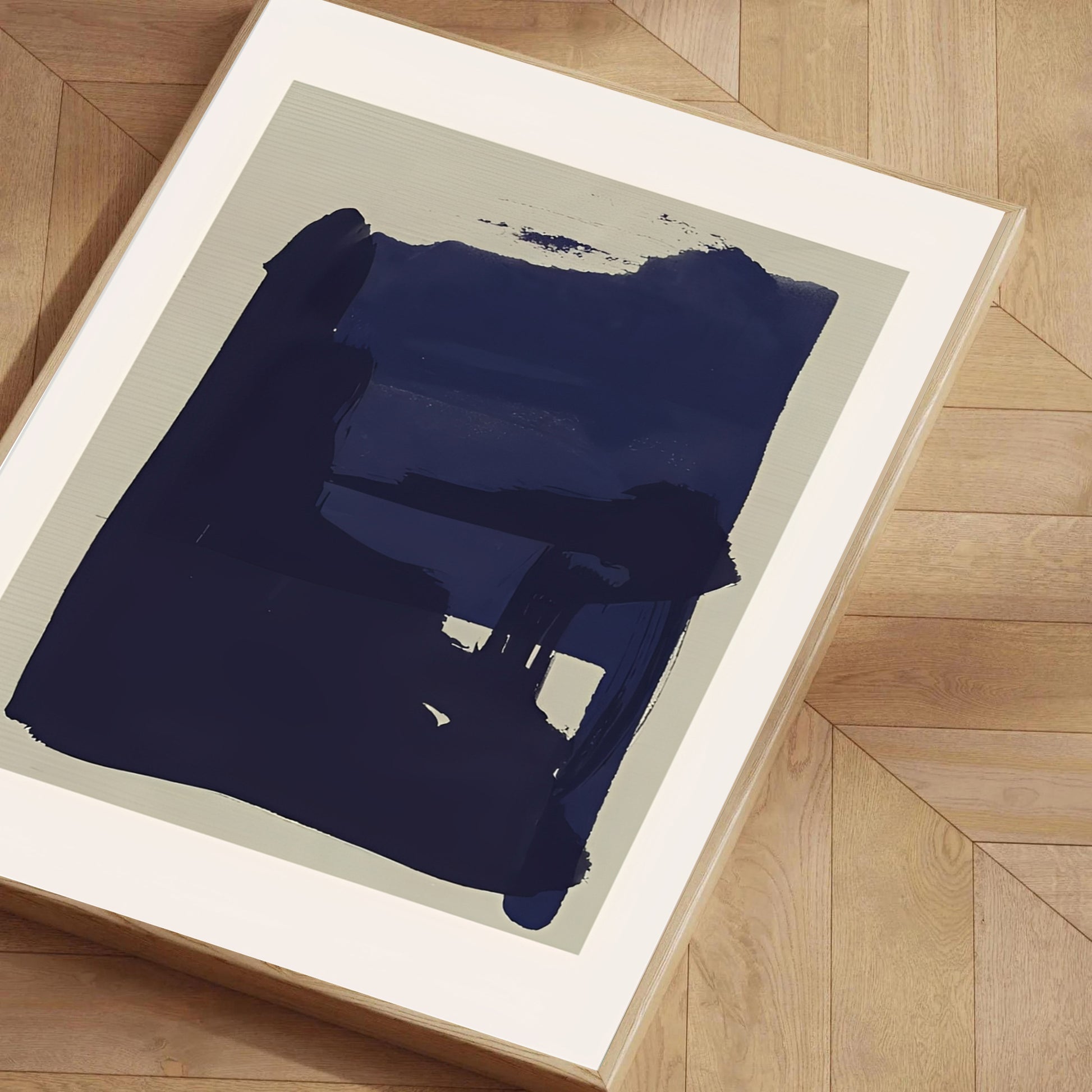 Framed abstract art piece with a large blue brushstroke on a beige background, displayed on a wooden floor.