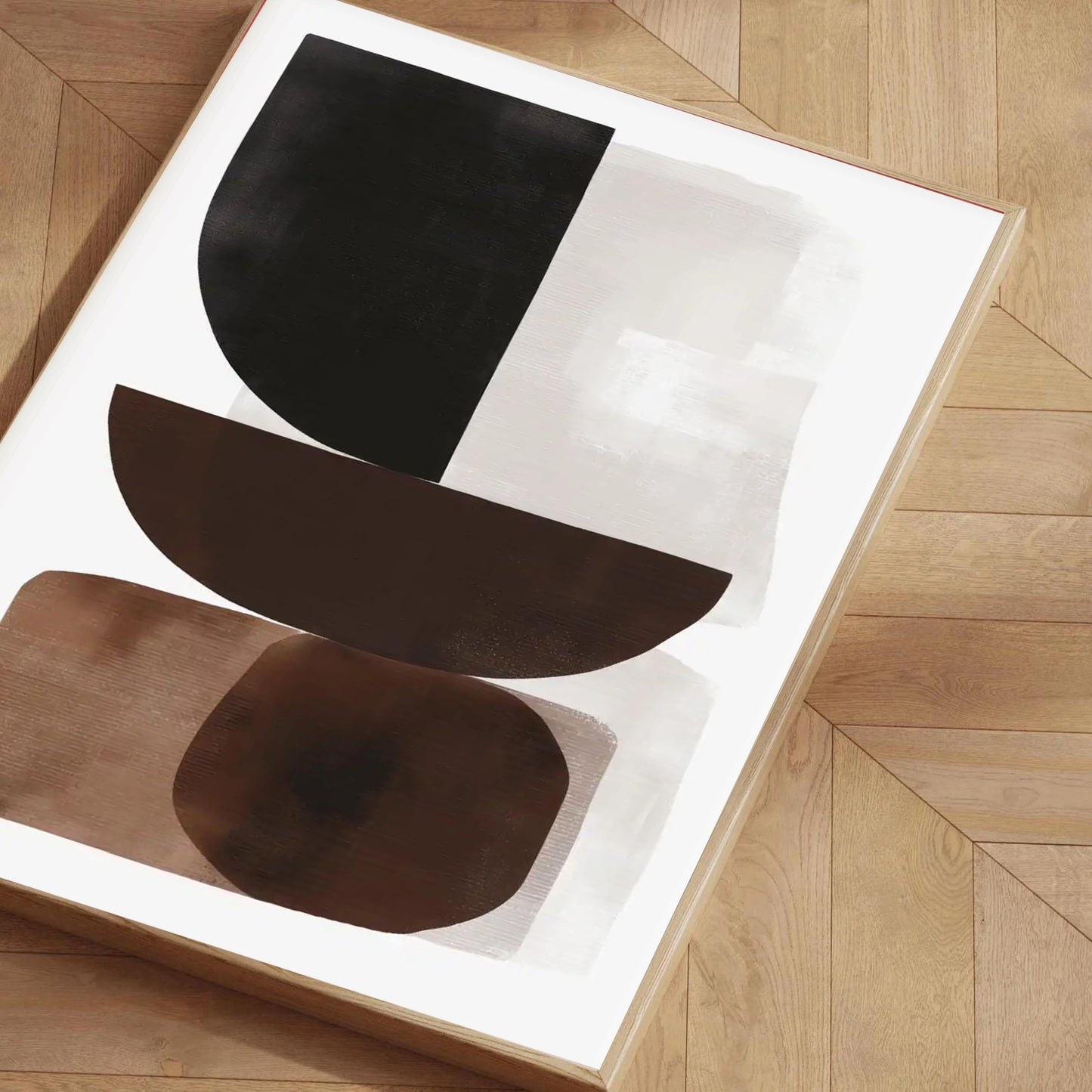 Abstract art piece with black and brown shapes on a white background, placed on a wooden floor.