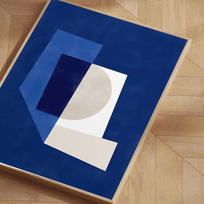 Abstract art print with geometric shapes on a blue background, placed on a wooden floor.