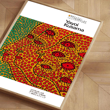 Framed poster inspired by Yayoi Kusama featuring colorful dotted abstract faces in red, yellow, and green, placed on a wooden floor