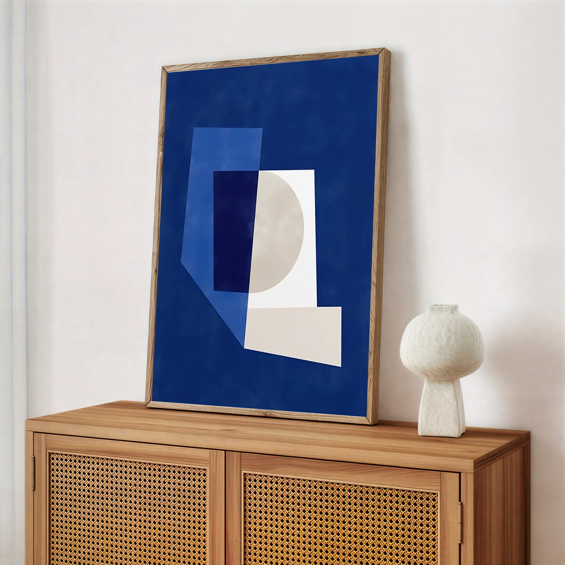 Abstract art piece on a wooden cabinet with a white vase.