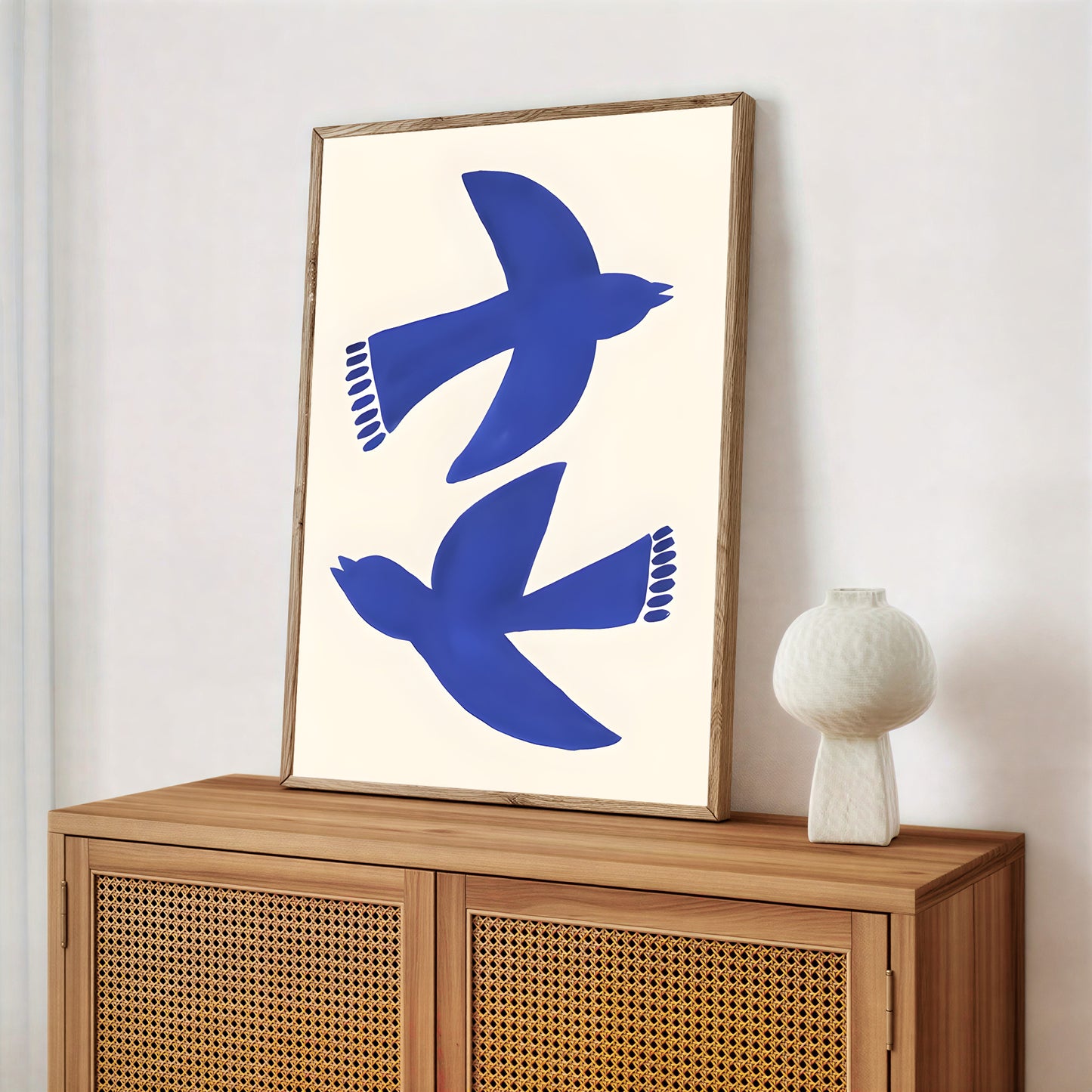 Framed artwork with blue birds on a white background above a wooden cabinet.