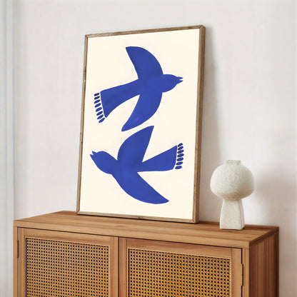 Framed artwork with blue birds on a white background above a wooden cabinet.