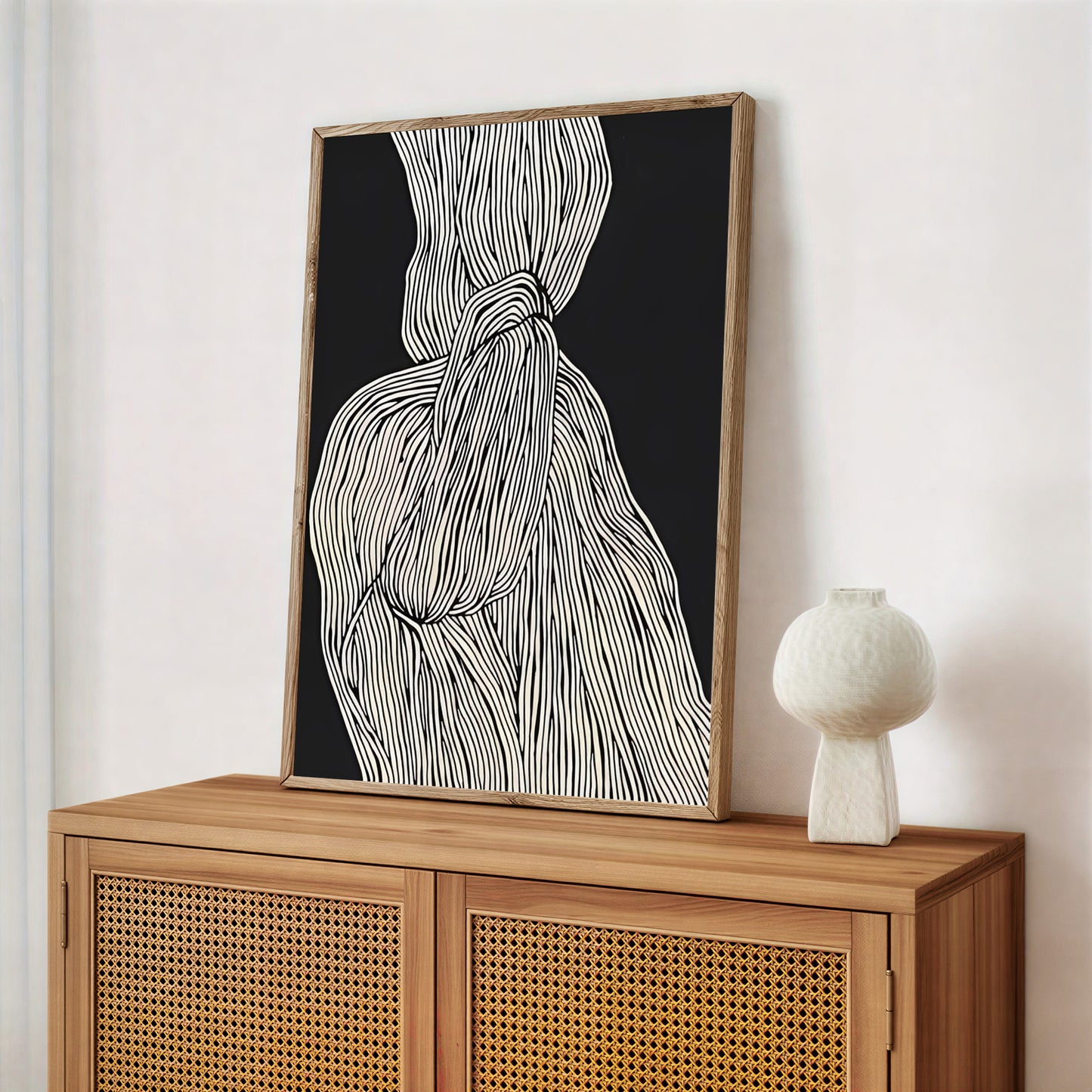 Framed abstract artwork on a wooden cabinet with a white vase.