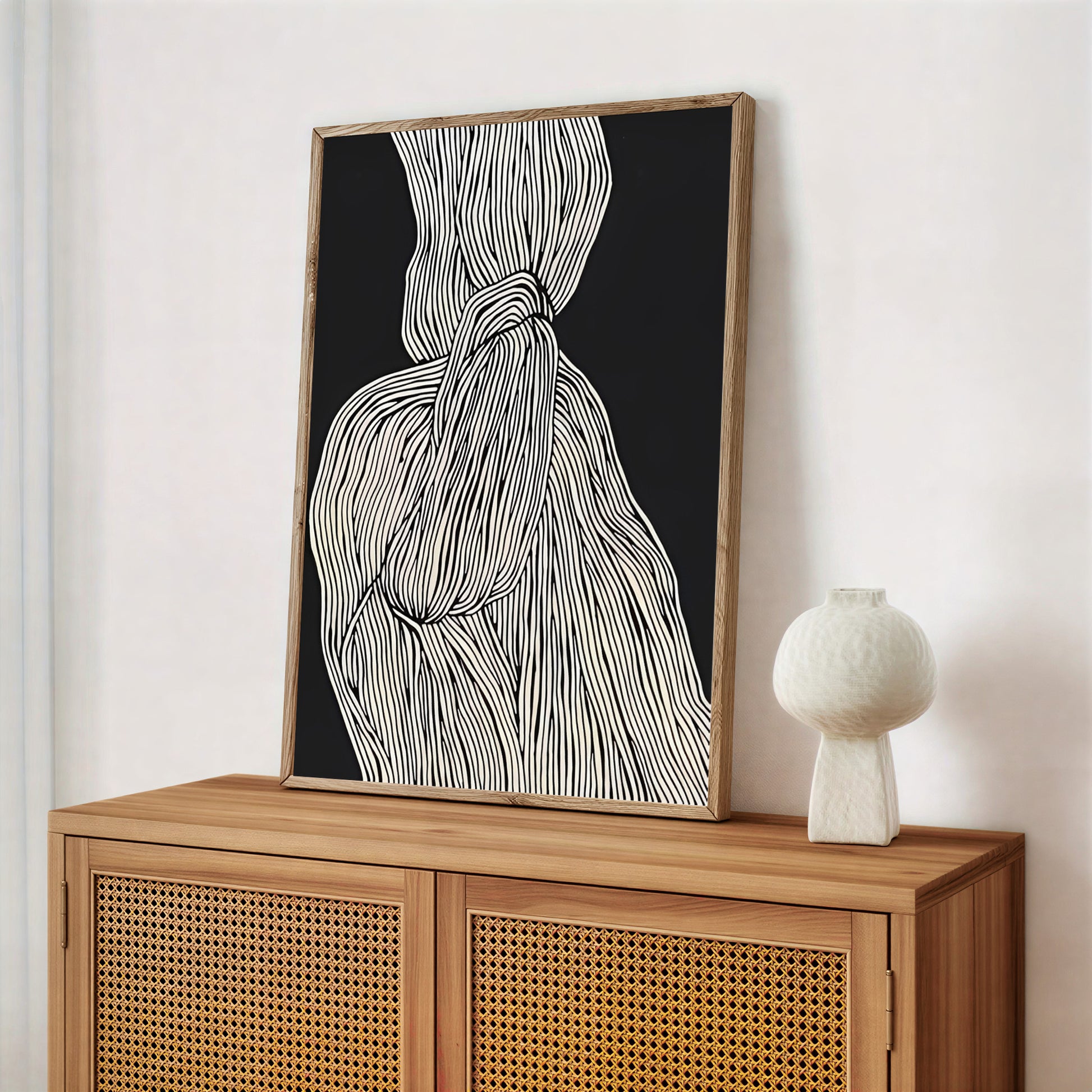 Framed abstract artwork on a wooden cabinet with a white vase.