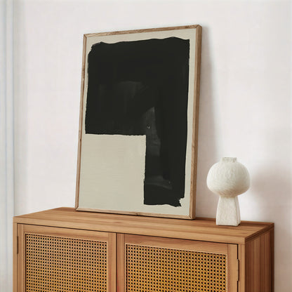 Framed abstract art on a wooden cabinet with a white vase.