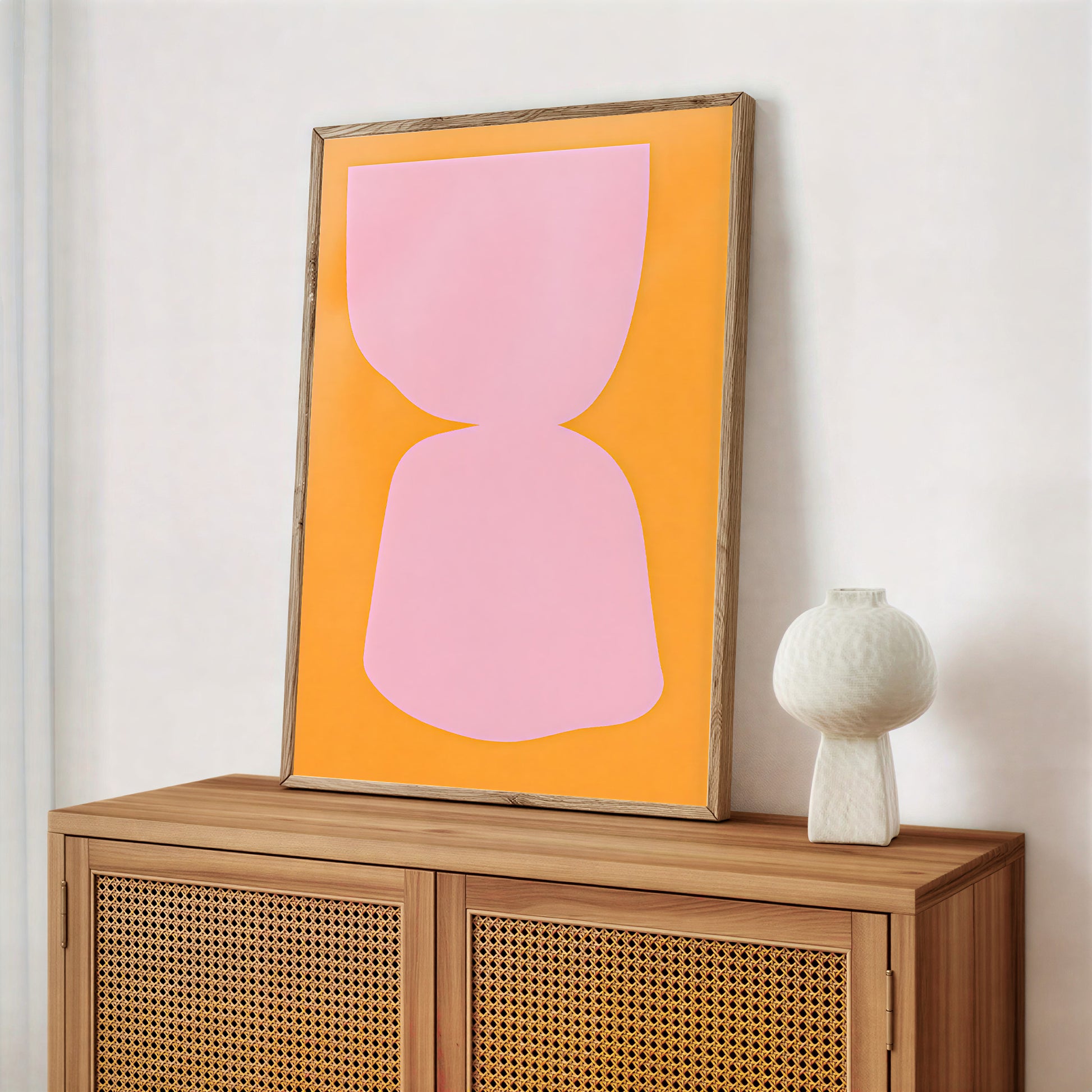 Framed abstract art with pink shape on orange background above a wooden cabinet.