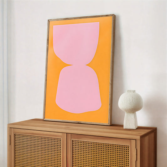 Framed abstract art with pink shape on orange background above a wooden cabinet.