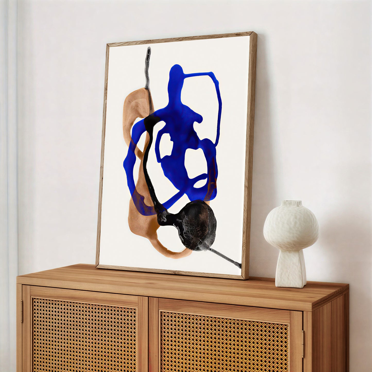 Abstract art piece with blue and black abstract shapes on a white background, framed and displayed on a wooden cabinet.