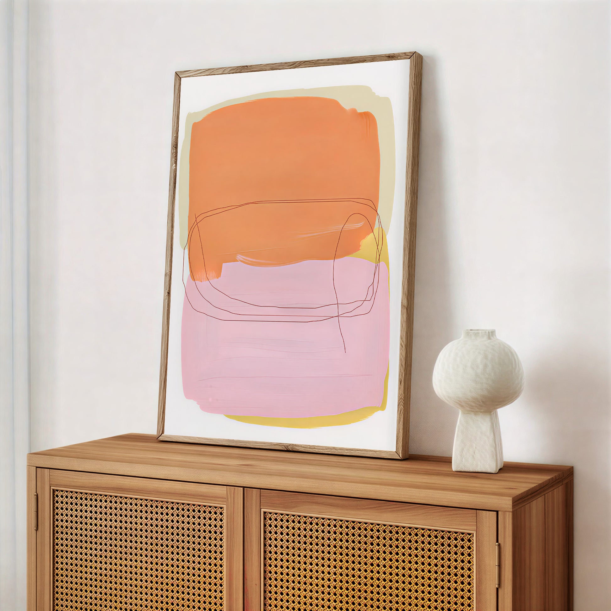 Abstract art print in a wooden frame on a wooden cabinet with a white vase.