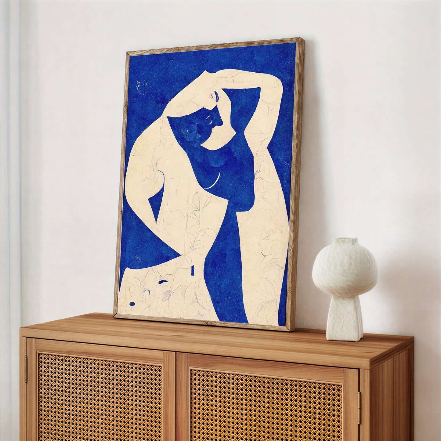 Framed artwork of a stylized figure on a wooden cabinet with a white vase.