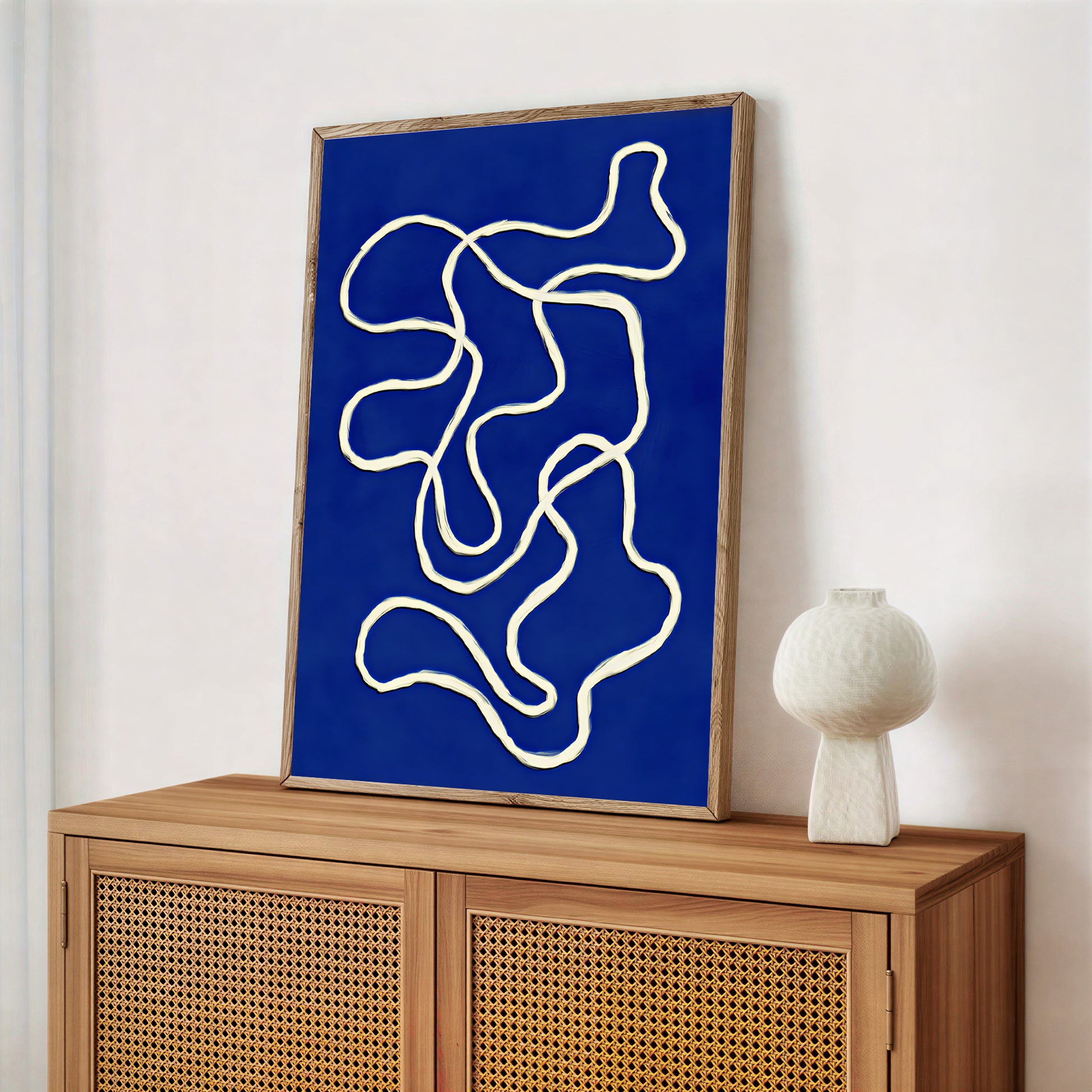 Abstract artwork with white lines on a blue background in a wooden frame, displayed on a wooden cabinet.