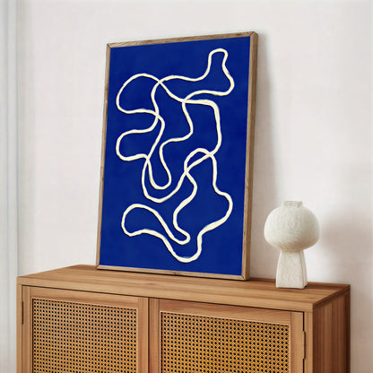 Abstract artwork with white lines on a blue background in a wooden frame, displayed on a wooden cabinet.