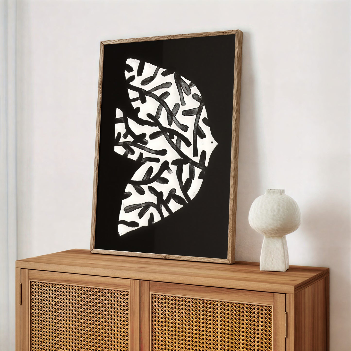 Framed abstract art piece on a wooden cabinet with a white vase.