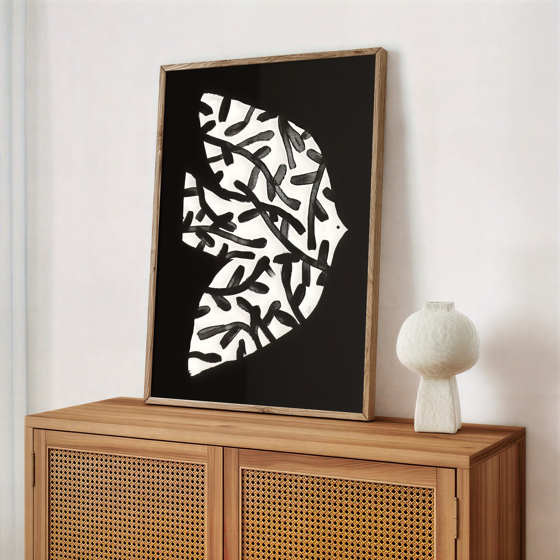 Framed abstract art piece on a wooden cabinet with a white vase.