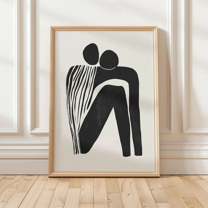 Framed abstract artwork of two black figures on a white background, displayed on a wooden floor with a white paneled wall.