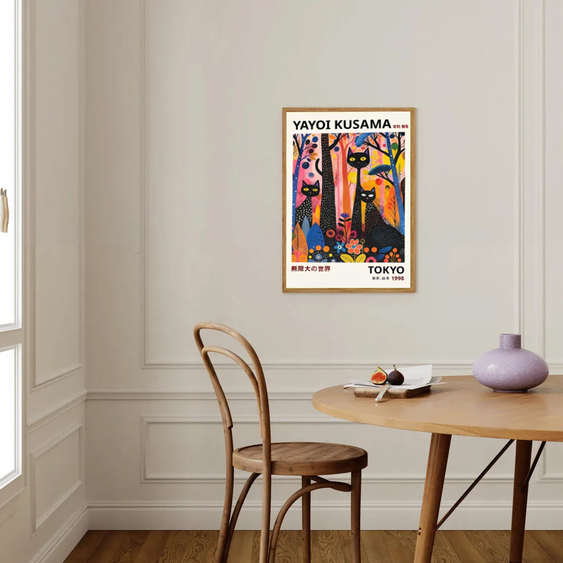 Colorful Yayoi Kusama cat poster 1996 on a wall above a wooden table with a vase and fruit bowl.