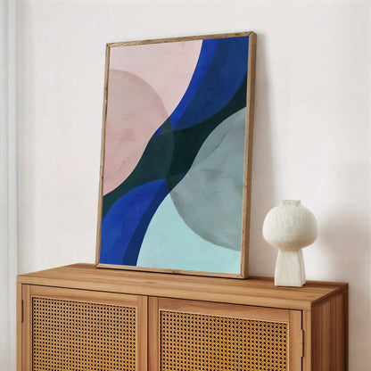 Abstract art piece on a wooden cabinet with a white vase.