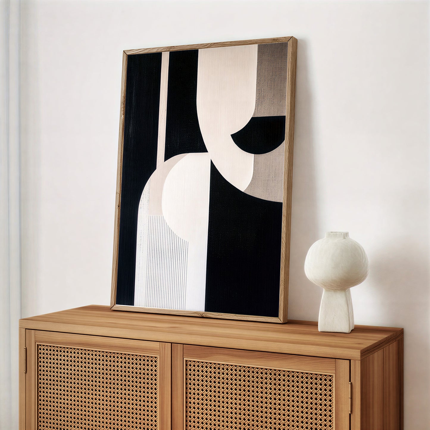 Abstract black and white painting in a wooden frame on a wooden cabinet with a white vase.