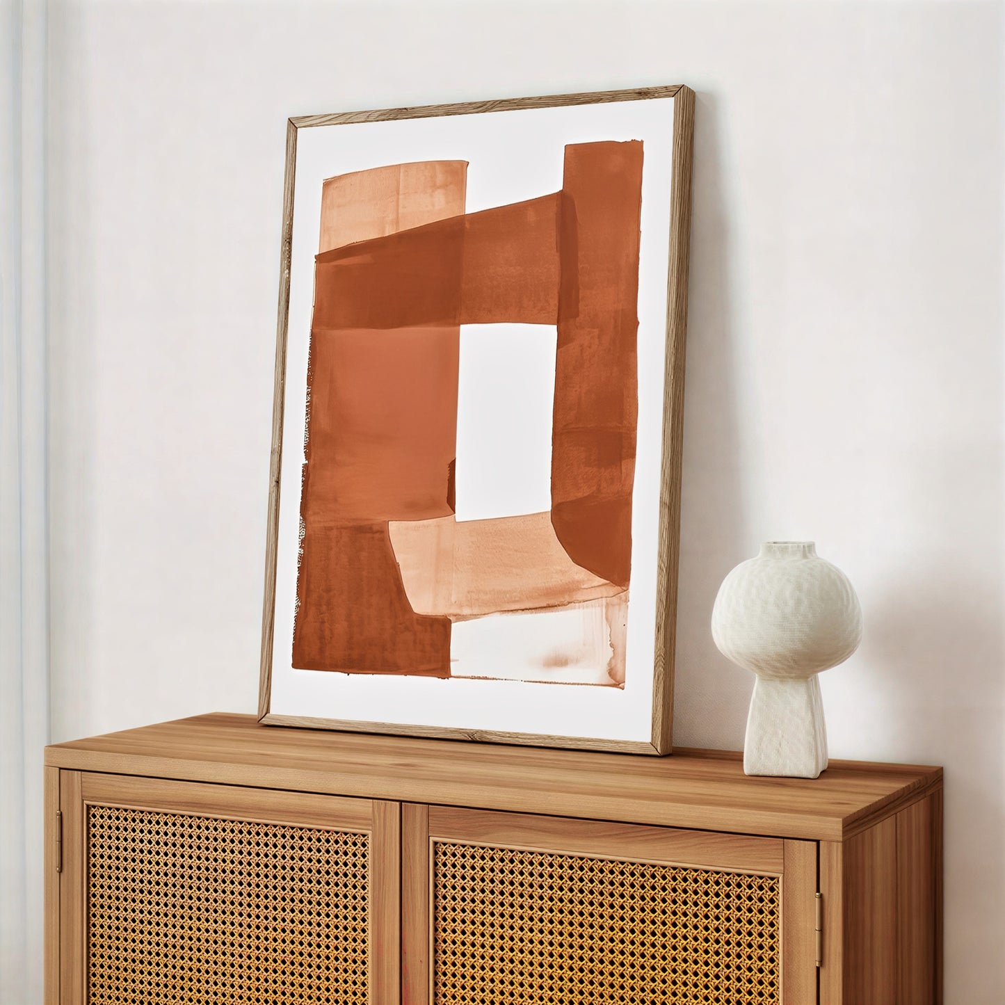 Abstract art piece on a wooden cabinet with a white vase.