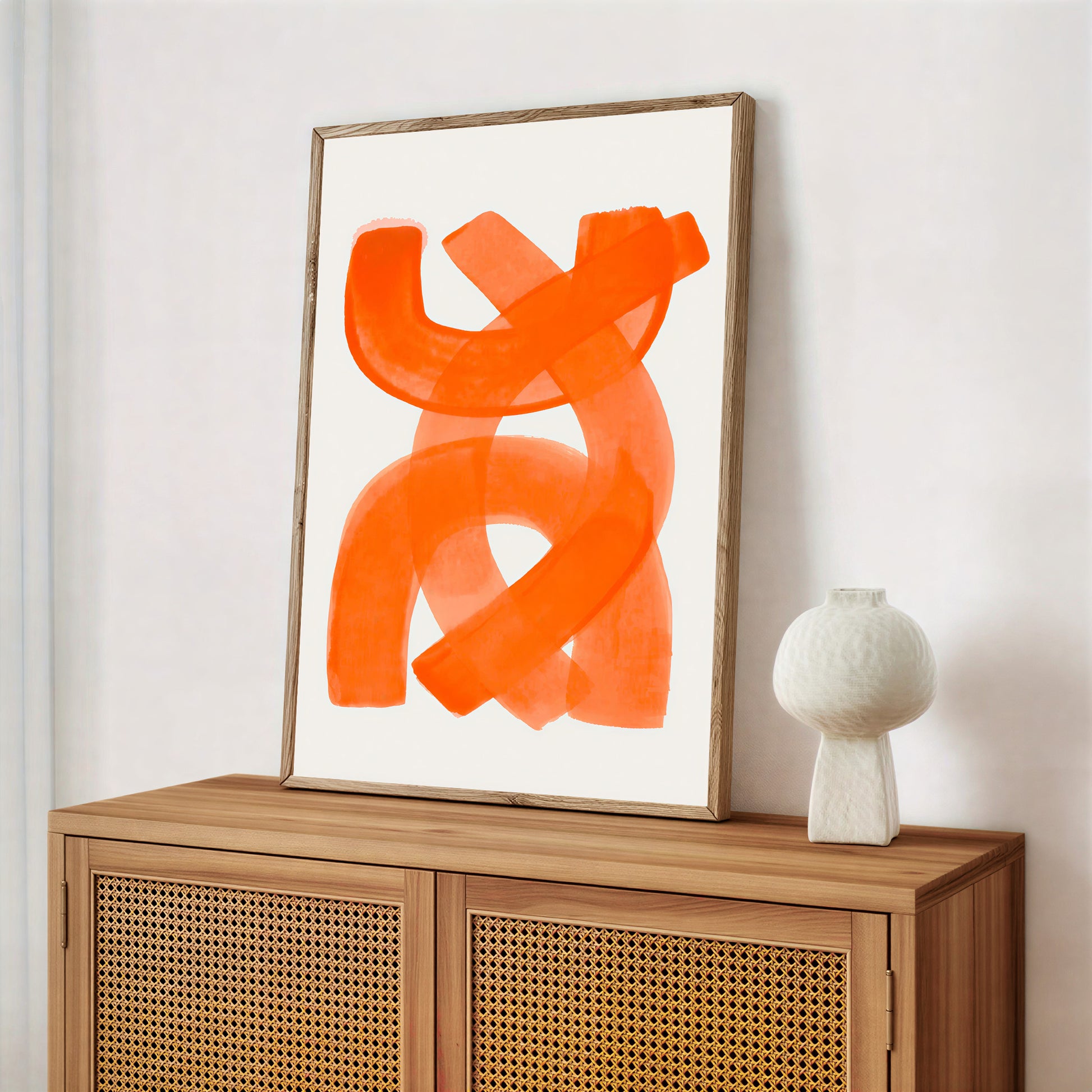 Abstract orange artwork on a white wall above a wooden cabinet with a decorative vase.