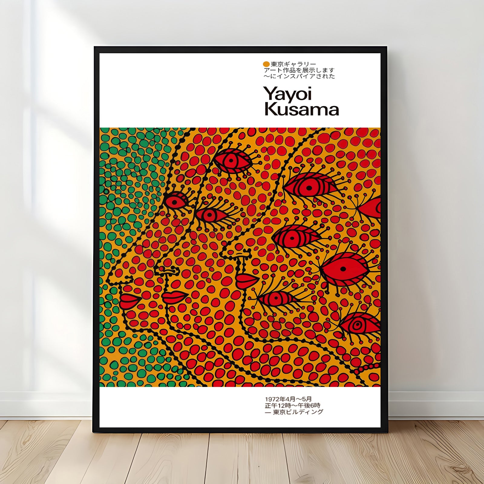 Yayoi Kusama–style framed poster with vibrant polka-dot abstract faces in red, yellow, and green, displayed upright against a sunlit white wall