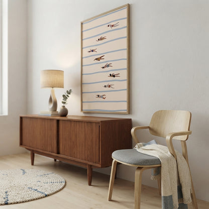 A framed Minimalist Swimming Pool Art Print in Scandi style with soft blue and peach tones, featuring horizontal blue stripes and small brown bird silhouettes, displayed above a mid-century wooden credenza in a bright, modern room with a wooden chair and a lamp.