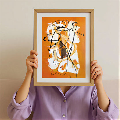 Person holding a framed abstract artwork with orange, white, and black colors against a beige background.