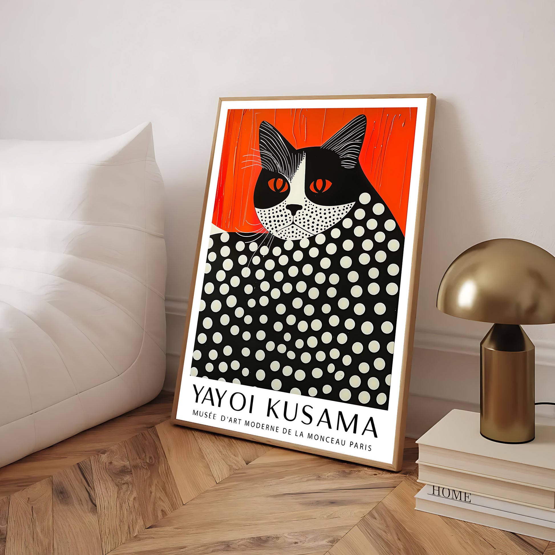 Yayoi Kusama cat print poster in gold frame leaning against a white wall beside a cozy sofa and brass lamp, modern home decor inspiration