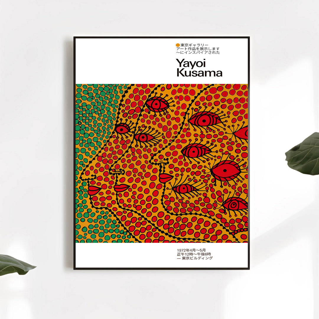 Minimalist display of a Yayoi Kusama–inspired art poster showing colorful dotted abstract faces, framed in black with decorative plant leaves nearby
