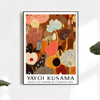 Framed artwork by Yayoi Kusama on a white wall with leaves.