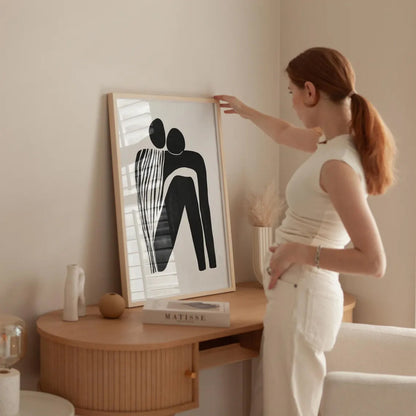Woman adjusting a framed artwork on a wall in a room with a wooden side table and decor items.