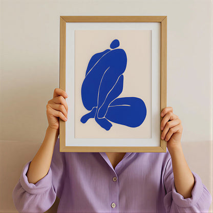 Person holding a framed abstract art print with blue shapes against a beige background