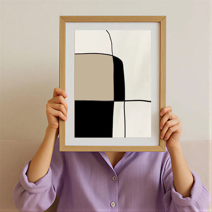 Person holding a framed abstract art print with geometric shapes against a plain background