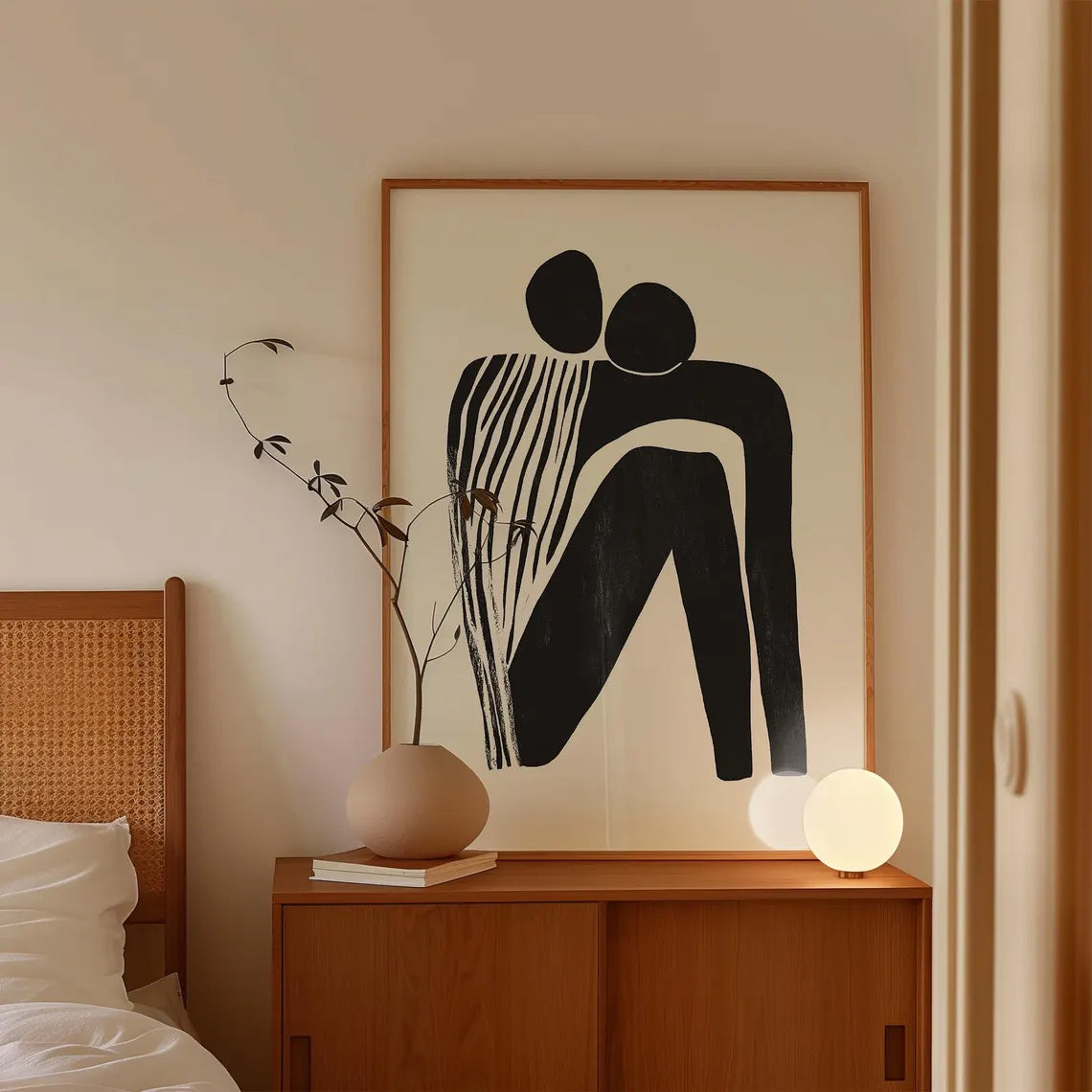 Framed abstract artwork of two figures on a wall above a wooden side table with decorative items.