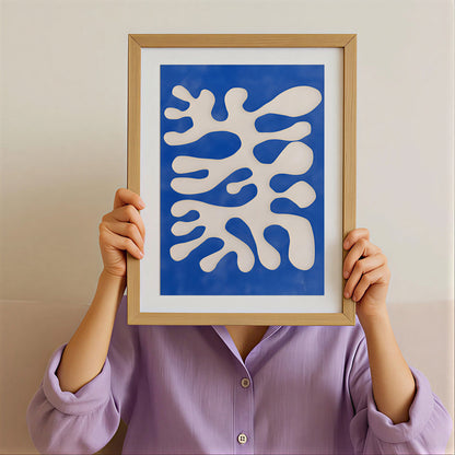 Person holding a framed abstract artwork with blue and white design against a plain background