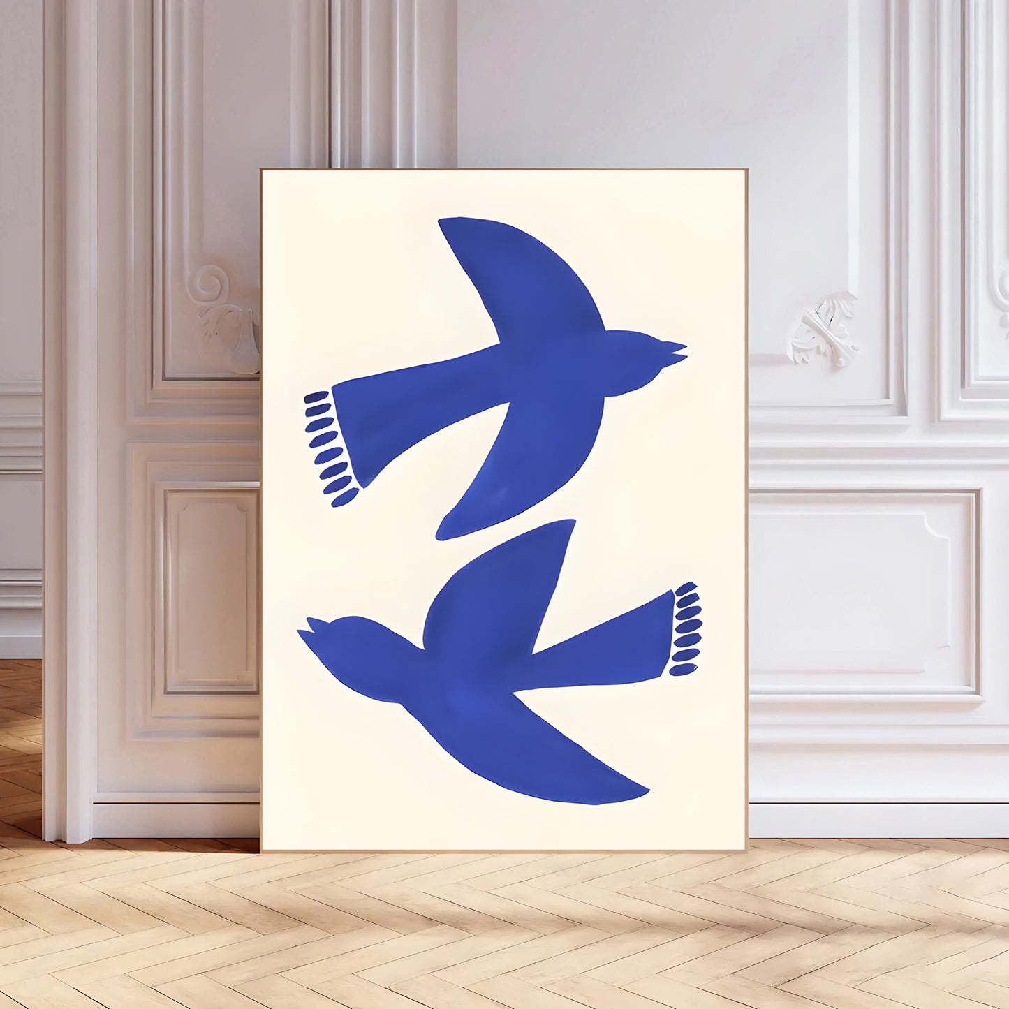 Framed artwork with blue bird silhouettes on a white background, displayed in a room with wooden flooring and white walls.