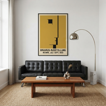 A Minimalist Geometric Bauhaus Exhibition Art Print – Minimalist Bauhaus Exhibition Wall Art  by PrintHaus with a mustard yellow background and black geometric design hangs above a black leather sofa in a modern living room with a wooden coffee table and floor lamp.
