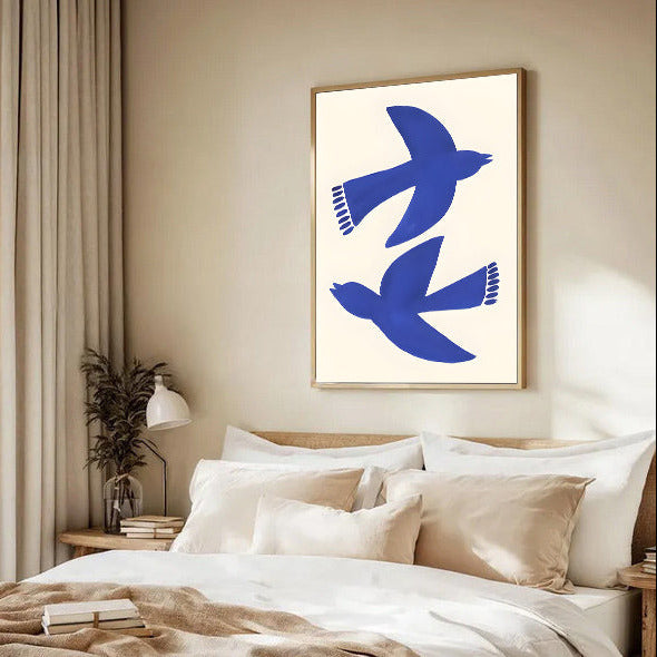 Modern bedroom with a bed, decorative pillows, and a framed abstract artwork of blue birds on the wall.
