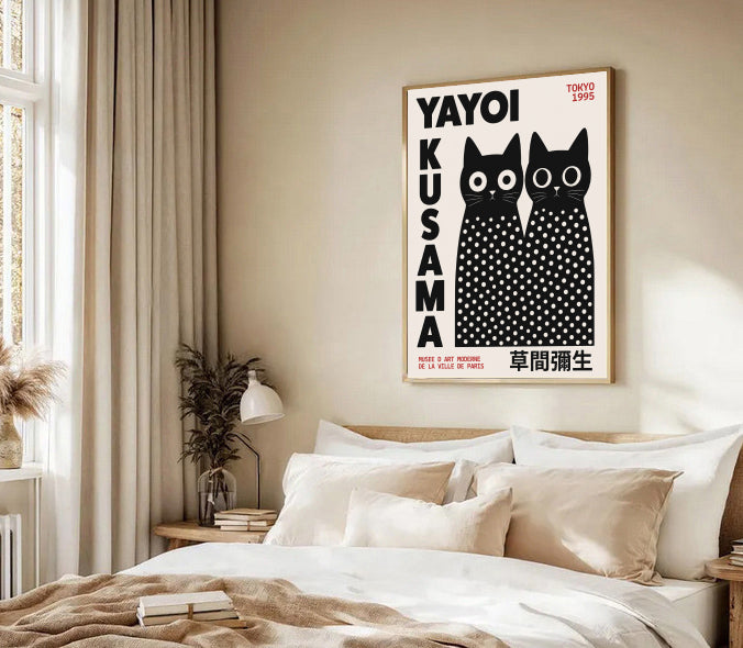 Framed artwork of black cats with text on a wall above a bed in a bedroom. Yayoi Kusama Inspired Black Cat Poster