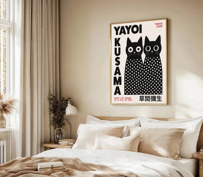 Framed artwork of black cats with text on a wall above a bed in a bedroom. Yayoi Kusama Inspired Black Cat Poster