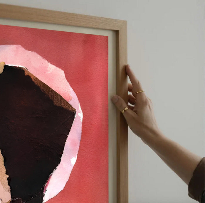 Person adjusting a framed artwork with a red and pink abstract design.