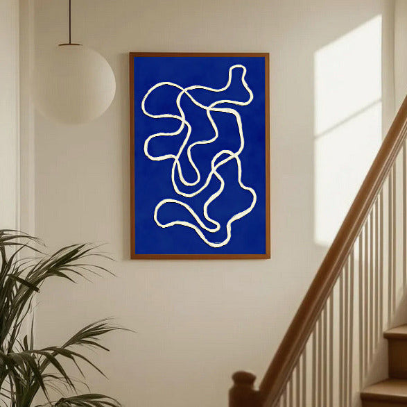 Abstract artwork with white lines on a blue background in a wooden frame, hanging on a wall near a staircase.
