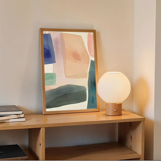 Abstract art print on a wooden shelf with a lamp and books.