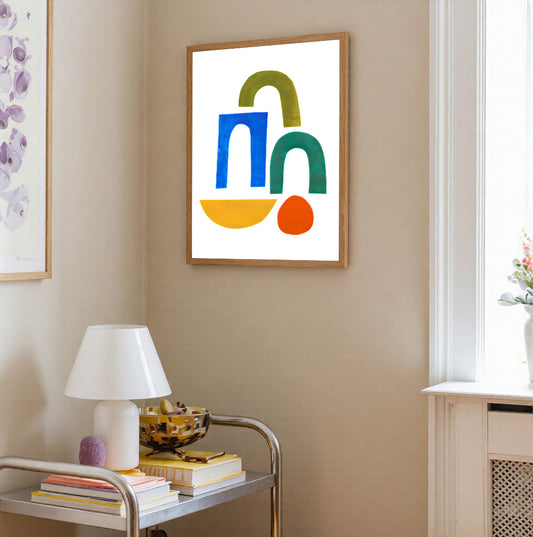 Colorful abstract art piece on a beige wall with a lamp and books on a table.